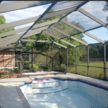 Gable-roofed screen enclosure over a pool and raised spa, viewed from inside the cage