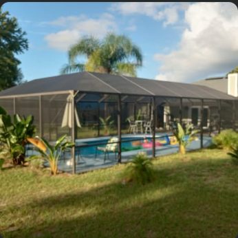 Screened pool cage seen across the lawn, pool and patio furniture visible through the mesh