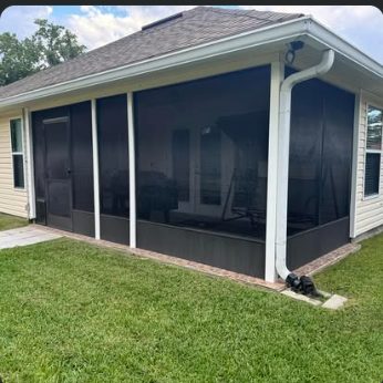 Screened rear porch on a stucco home with a shingle roof and downspout